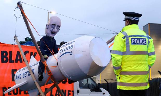 Policial olha para uma pessoa usando uma máscara que representa o fundador da Amazon, Jeff Bezos, enquanto os ativistas da Extinction Rebellion bloqueiam a entrada de um centro de atendimento da Amazon em Tilbury, Essex Foto: HENRY NICHOLLS / REUTERS