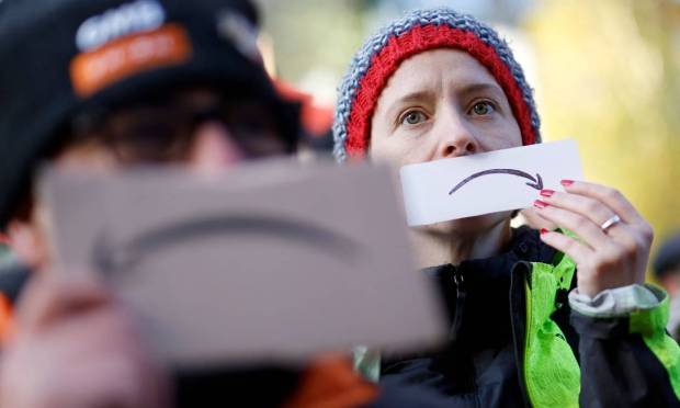 Ativistas seguram logo da Amazon de ponta-cabeça para protestar contra a gigante do vareja no centro de Londres Foto: TOLGA AKMEN / AFP